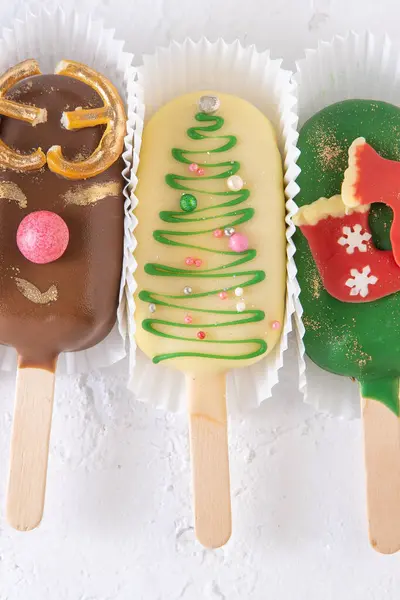 Christmas dessert. Sweet food. Cheesecake on a stick in the shape of ice cream. Childrens treat in winter. Candy Christmas tree, snowman, deer and Santa Claus. Gingerbread cookies. White background.