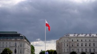 Mavi gökyüzünde rüzgarda dalgalanan Polonya bayrağı. Bulutlarda Lehçe beyaz kırmızı bayrak. Meydanda bayrak direği. Sokaktaki evler..