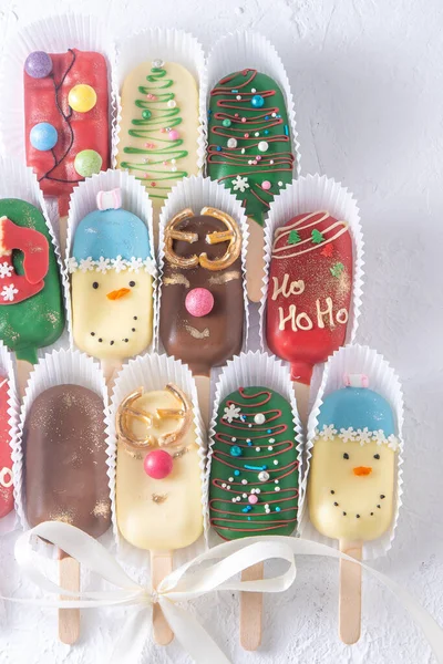 Christmas dessert. Sweet food. Cheesecake on a stick in the shape of ice cream. Childrens treat in winter. Candy Christmas tree, snowman, deer and Santa Claus. Gingerbread cookies background.