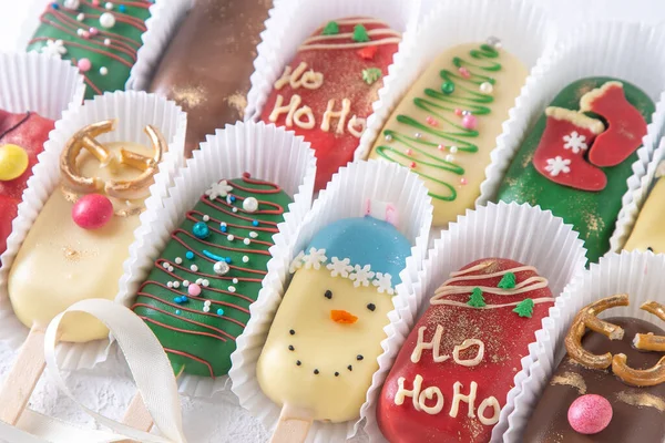 Christmas dessert. Sweet food. Cheesecake on a stick in the shape of ice cream. Childrens treat in winter. Candy Christmas tree, snowman, deer and Santa Claus. Gingerbread cookies background.