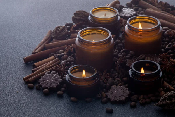 Soy scented candle in a jar. Coffee beans, anise, cinnamon spices. The candles are burning. Dark background