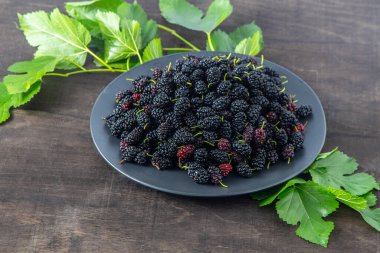 Bir kasede dut. Yazın böğürtlen hasadı. Meyveli siyah gıda arka planı. Dut yapraklı yeşil dal. Yaprak masanın üstünde..