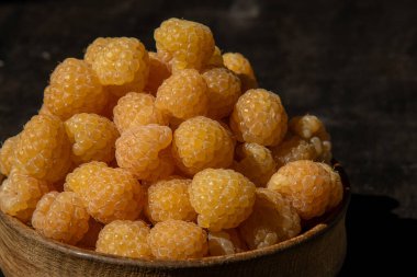 Masanın üzerindeki ahşap kasede sarı ahududular. Yaz meyveleri arka planı. Vitamin yiyecekleri, böğürtlen hasadı. Sağlıklı beslenme.