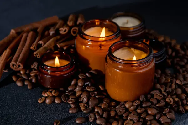 Soy scented candle in a jar. Coffee beans, anise, cinnamon spices. The candles are burning. Dark background