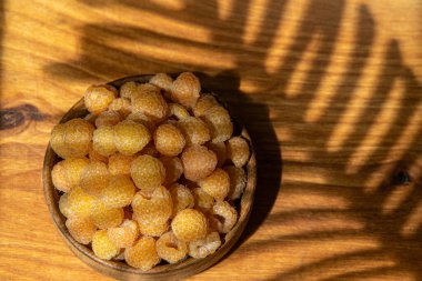 Masanın üzerindeki ahşap kasede sarı ahududular. Yaz meyveleri arka planı. Vitamin yiyecekleri, böğürtlen hasadı. Sağlıklı beslenme.