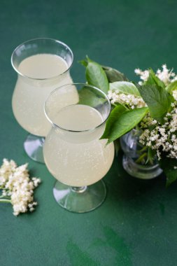 Karbonatlı mürver çiçeği içeceği. Gözlüklü yaz kvass 'ı. Ev yapımı köpüklü hugo suyu. Buza yeşil arka planda iki kadehte içiyor.