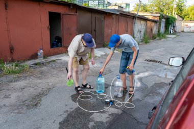 Baba ve genç oğlu garajın yanındaki sokakta birlikte çalışıyorlar. Açık hava aktivitesi. Aile zaman geçirir. Yardım etmek ve öğretmek. Plastik şişeden araba yıkamak için hortum ve pompa tamir etmek..