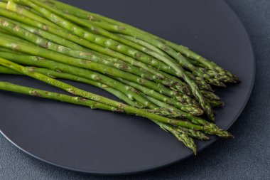 Bir sürü yeşil kuşkonmaz. Taze bahar sebzeleri ızgarada. Siyah tabak..