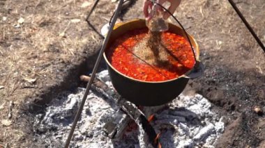 Çorbanın içine baharat serpin. Yürürken kamp ateşinde kırmızı Ukrayna çorbası pişir. Ateşin üstünde yemek pişirmek. Kazan dışarıda..
