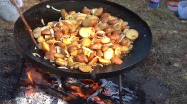Kamp ateşinde yürüyüş yaparken yemek pişirmek. Kızarmış patates ve soğan karışımı. Dışarıdaki yangında kızartma tavası. Doğada sokak yemeği.