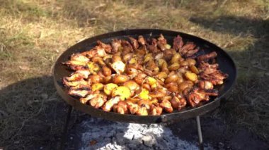 Kamp ateşinde yürüyüş yaparken yemek pişirmek. Kızarmış patates. Dışarıdaki yangında kızartma tavası. Doğada sokak yemeği. Tavuk kanadı. Sebzeli ızgara et.