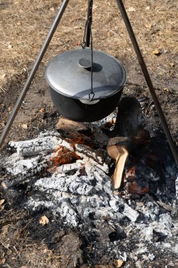 Kapaklı kamp tenceresi. Yürüyüşte kamp ateşinde yemek pişirmek. Ateş kömürü yakacak odun alevi. Caldron tripod gerçekçiliği dışarıda pişiyor..