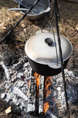 Kapaklı kamp tenceresi. Yürüyüşte kamp ateşinde yemek pişirmek. Ateş kömürü. Caldron gerçekçiliği dışarıda pişiyor. Yakacak odun ateşi yanıyor.