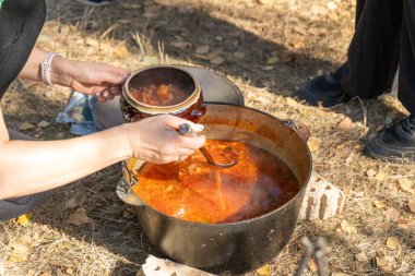 Ateşin üstünde kırmızı Ukrayna Borscht 'u pişirmek. Kamp yemeği. El kaşığı. Yürürken ahşap üzerinde yemek yapmak. Açık hava yaz kampı. Çanak çömlek tabağı.