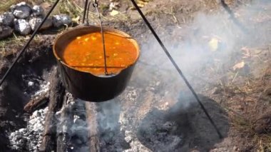 Yürürken kamp ateşinde kırmızı Ukrayna çorbası pişir. Ateşin üstünde yemek pişirmek. Kazan açık hava yemeği.