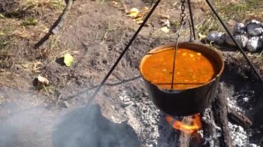 Yürürken kamp ateşinde kırmızı Ukrayna çorbası pişir. Ateşin üstünde yemek pişirmek. Kazan, kampın dışında sıcak yemek.