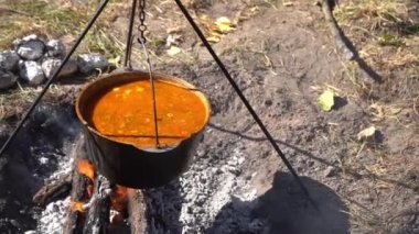 Yürürken kamp ateşinde kırmızı Ukrayna çorbası pişir. Ateşin üstünde yemek pişirmek. Kazan açık hava turizmi