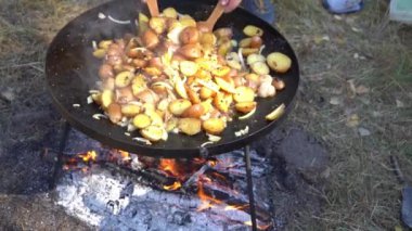 Kamp ateşinde yürüyüş yaparken yemek pişirmek. Kızarmış patates soğanı. Dışarıdaki yangında kızartma tavası. Doğada sokak yemeği.
