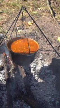 Yürürken kamp ateşinde çorba pişir. Ateşin üstünde yemek pişirmek. Kazan bowlingci çömleği