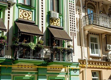 Gölge çadırlı yeşil balkon. Tencerede çiçekler olan renkli ev cephesi