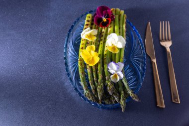 Bir sürü yeşil kuşkonmaz. Mavi tabakta taze bahar sebzesi. İbne çiçekleri. Kuşkonmaz ızgara yemek, karanlık fotokopi alanı arka planı