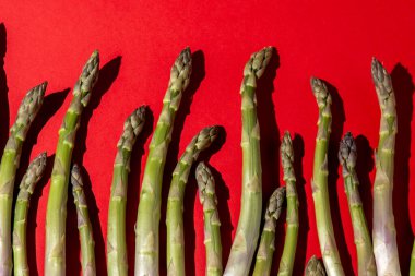 Kırmızı arka planda yeşil kuşkonmaz. Sebzeli yiyecek manzarası. Taze filizler.