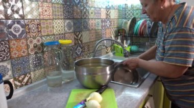 Yaşlı bir kadın mutfak lavabosunda tencere yıkıyor. Ev ödevi