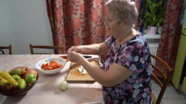 Yaşlı bir kadın mutfakta soğan doğruyor ve evde salata hazırlıyor. Eski eller ve bıçak yakın çekim. Tahta tahta. Sebze. Sağlıklı beslenme