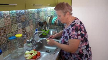 Yaşlı bir kadın mutfakta biber kesip yıkar ve evde salata hazırlar. Eller ve bıçak yakın. Tahta tahta. Sebze. Sağlıklı beslenme