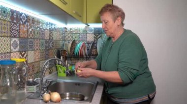 Yaşlı bir kadın patates soyar. Mutfak lavabosunda patates püresi. Evde sebze pişir. Yemek hazırlama.