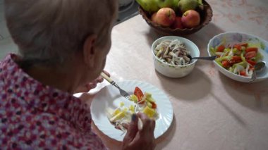 Emekli yaşlı kadın akşam yemeğini tabakta yiyor. Sağlıklı yiyecekler. Balık ve sebze. Masa ve eller çatal ve bıçakla yakın plan.