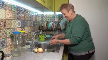 Yaşlı bir kadın patates soyar. Mutfak lavabosunda patates püresi. Evde sebze pişir. Yaşlı büyükanne.