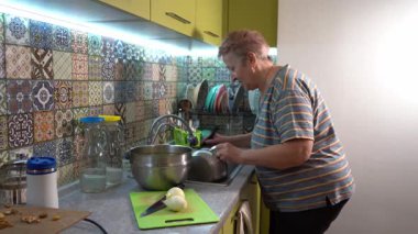 Yaşlı bir kadın evdeki mutfaktaki lavaboda tencereyi yıkıyor. Bulaşıkları yıkıyorum. Yemek pişirmek.