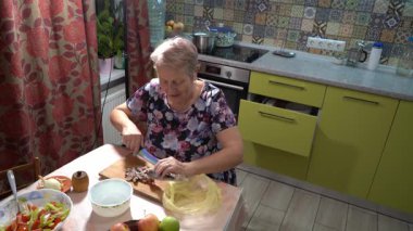 Yaşlı bir kadın mutfakta balık yemeği hazırlıyor. Tahtayı kesiyor. Ringa balığı