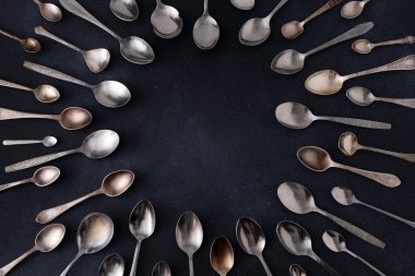 Farklı kaşıklar. Siyah arka planda gümüş çatal bıçak seti. Kaşığı masaya koy. Çember çerçeve üst görünüm kopyalama alanı gereci.