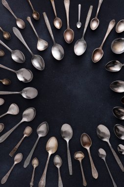 Farklı kaşıklar. Siyah arka planda gümüş çatal bıçak seti. Kaşığı masaya koy. Çember çerçeve üst görünüm kopyalama alanı. Eski sofra takımı servisi.