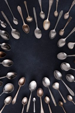 Farklı kaşıklar. Siyah arka planda gümüş çatal bıçak seti. Kaşığı masaya koy. Çember çerçeve üst görünüm kopyalama alanı. Eski çatal bıçak takımı