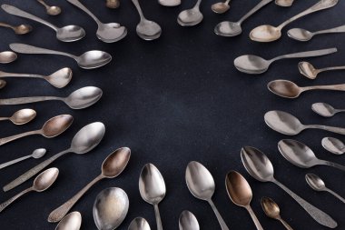 Farklı kaşıklar. Siyah arka planda gümüş çatal bıçak seti. Kaşığı masaya koy. Çember çerçeve üst görünüm kopyalama alanı
