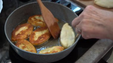 Büyükannenin elleri kızgın yağda kızartılmış tavada mini turtaları çevirir. Kızarmış turta, ev yapımı hamur yemeği. Soba evi.