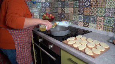 Bir kadın turta kızartmak için tavaya ayçiçeği yağı döker. Evde kızarmış yemek pişirmek. Büyükanne mutfakta aşçı.
