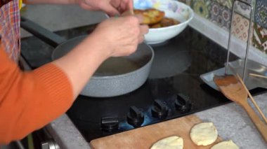 Büyükannem kızgın yağda turta pişiriyor. Tavada kızartılmış turta, ev yapımı hamur yemeği. Kadın mutfakta yemek pişiriyor. Eller