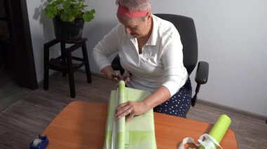 Makasla kes. Yaşlı bir kadın hediyesini yeşil kağıda sarar. Bir büyükanne evde bir kutu toplar. Eller yukarı görünüm