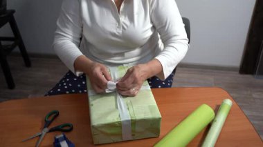 Yaşlı bir kadın hediyesini yeşil kağıda sarar. Bir büyükanne evde bir kutu toplar. Eller yukarı görünüm