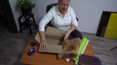 Yaşlı bir kadın hediyesini yeşil kağıda sarar. Bir büyükanne evde bir karton kutu paketler. Eller yukarı görünüm