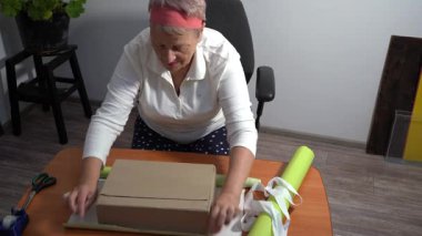 Yaşlı bir kadın hediyesini yeşil el sanatları kağıdına sarar. Bir büyükanne evde bir kutu toplar. Eller masa üstü görünümü