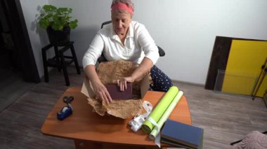 Taşınmak ve hediye olarak kitap paketlemek. Yaşlı bir kadın hediyesini yeşil kağıda sarar. Bir büyükanne evde bir kutu toplar. Eller yukarı görünüm