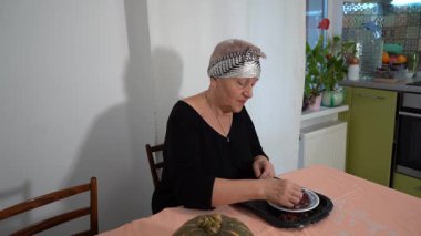 Yaşlı bir kadın kurutulmuş böğürtlen ayırıyor. Bir büyükanne mutfaktaki masada yemek hazırlar. Ev