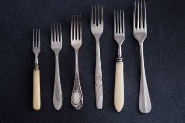 Siyah arka plandaki çatallar. Yemek için farklı çatal bıçak takımı. Gümüş çatal. Çeşitli Boyutlarda Vintage Koleksiyonu üst görünüm