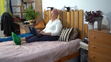 Dizüstü bilgisayarı olan aktif, yaşlı bir kadın evde yatağında otururken iletişim kuruyor ve çalışıyor. Yazan bir büyükanne.