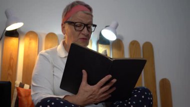 Yaşlı bir kadın yatakta oturmuş posta pullarından oluşan bir albüme bakıyor. Büyükannem evde sesli bir kitap okur..